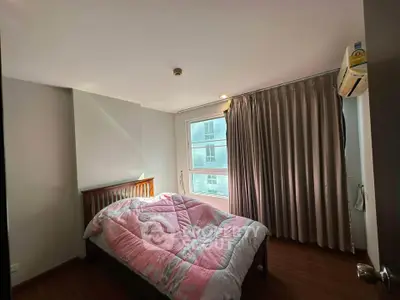 Cozy bedroom with wooden flooring and large window, featuring a pink comforter and elegant curtains.