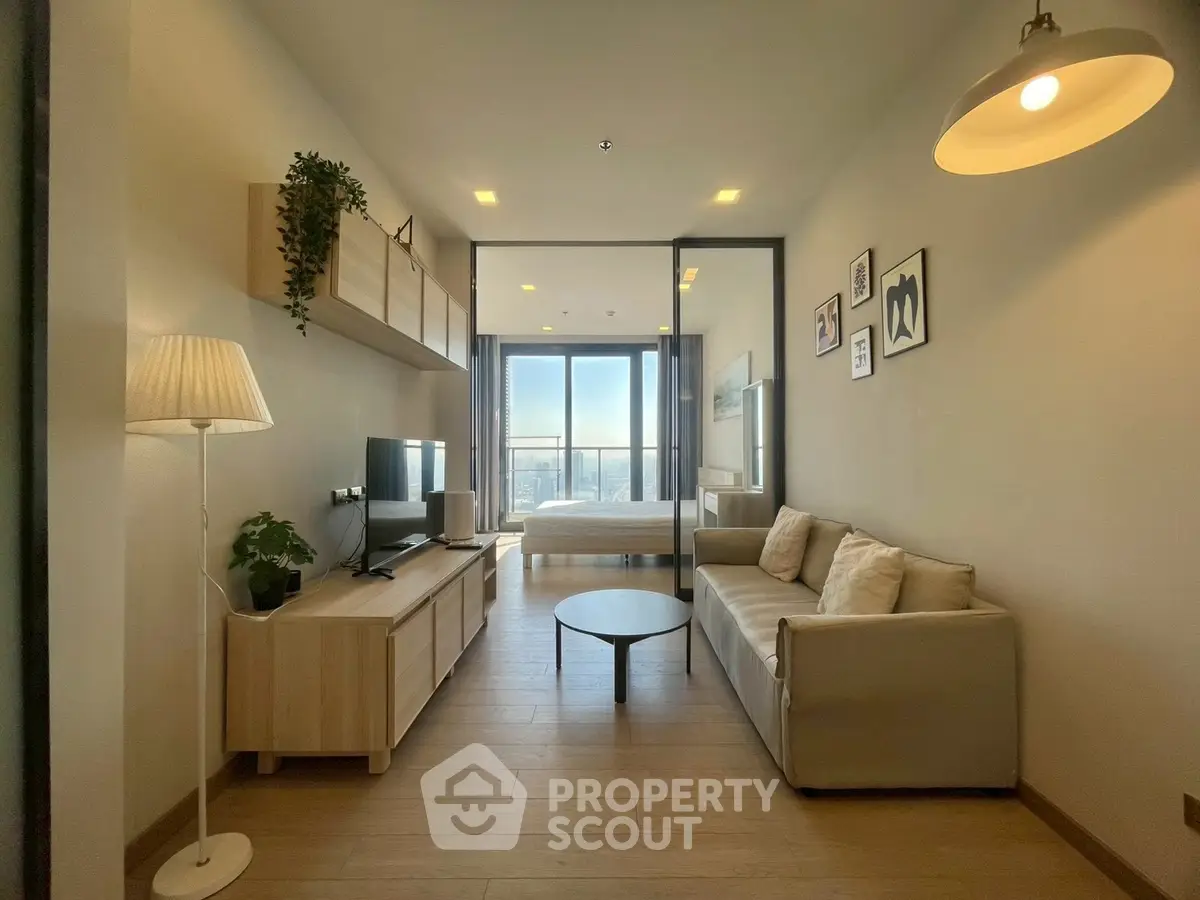 Modern open-plan living room with cozy sofa and stylish decor, leading to a bright bedroom with city views.