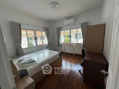 Spacious bedroom with wooden flooring, large windows, and modern furnishings in a serene residential setting.