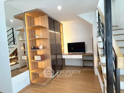Modern living room with stylish wooden shelving and staircase, featuring a sleek TV setup.