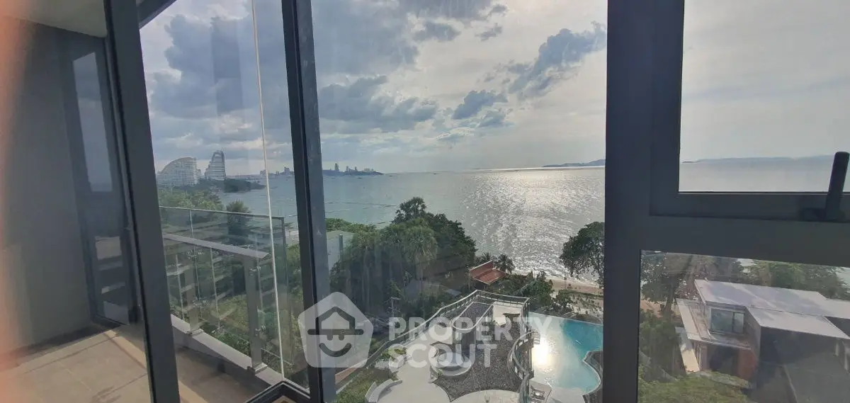 Stunning ocean view from high-rise apartment with glass balcony overlooking pool and lush greenery.