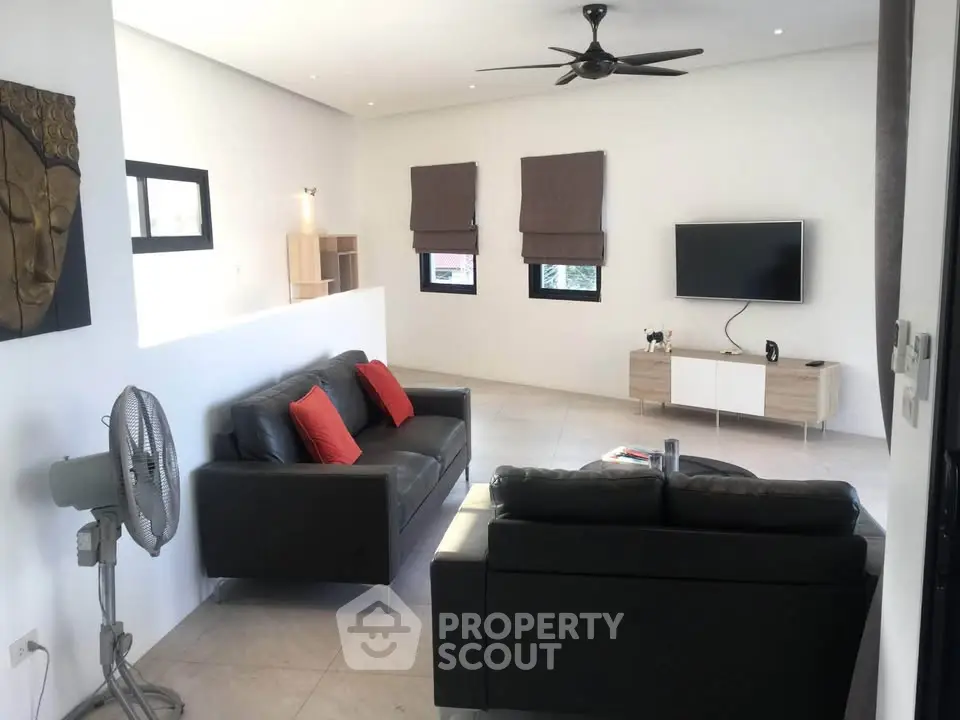 Modern living room with sleek black sofas, wall-mounted TV, and ceiling fan in a bright, minimalist design.
