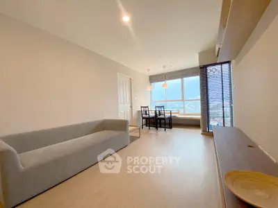 Spacious living room with ample natural light, modern furniture, and a cozy dining area leading to a sunlit balcony with a view.