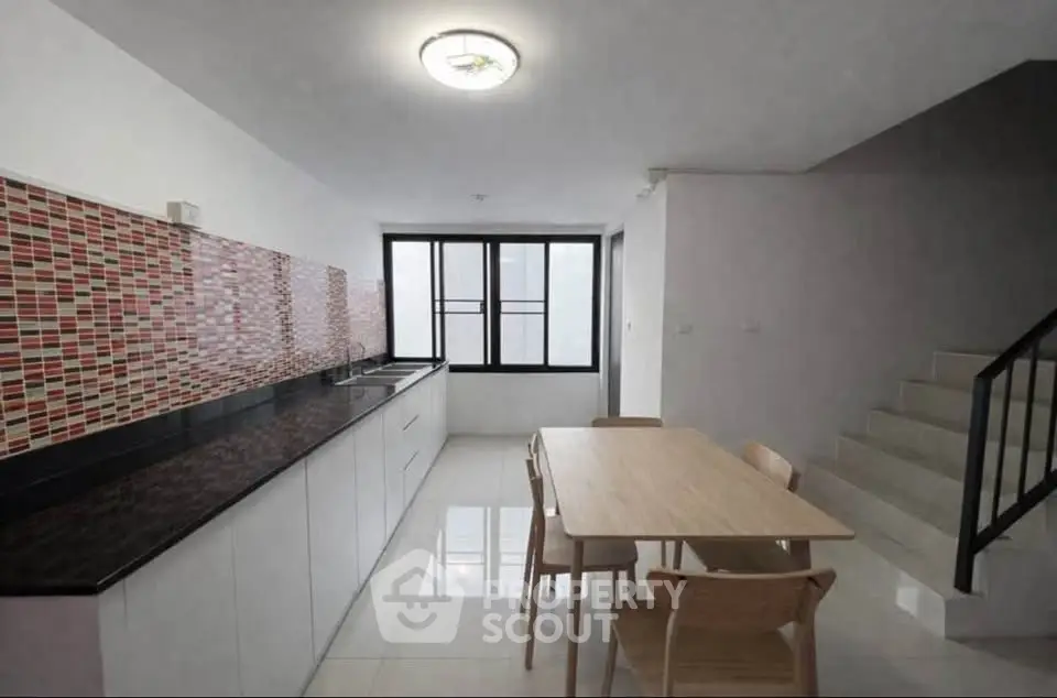 Modern kitchen with sleek design and dining area, featuring stylish backsplash and ample natural light.