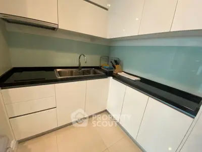 Modern kitchen with sleek white cabinets and black countertops, featuring a stainless steel sink and glass backsplash.