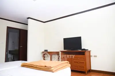 Spacious bedroom with TV and wooden furniture, ideal for relaxation.