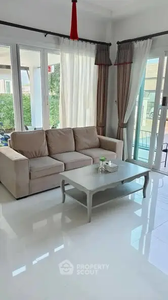 Bright and spacious living room with modern sofa and large windows, offering a serene view of the garden.