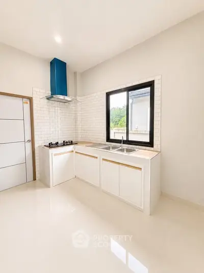 Modern kitchen with sleek white cabinetry and gas stove, featuring a large window for natural light.