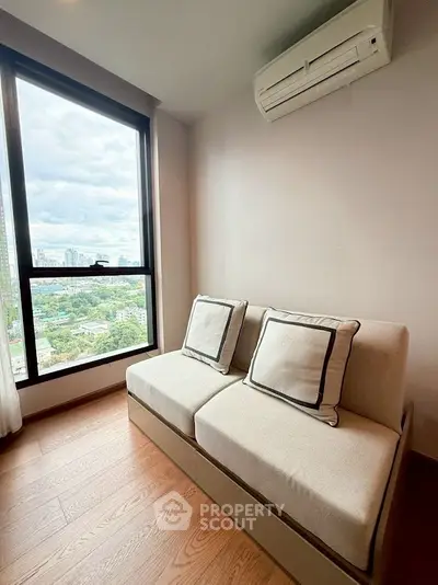 Cozy living room with large window and air conditioning, offering a serene city view.