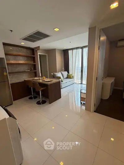 Modern open-layout living room with kitchen and dining area, featuring sleek furniture and large windows.