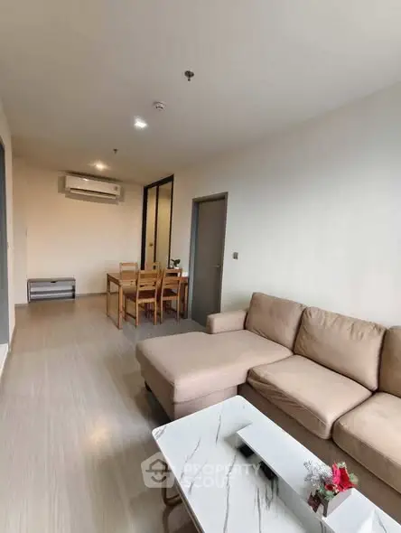 Spacious modern living room with beige sofa and dining area in open layout apartment.