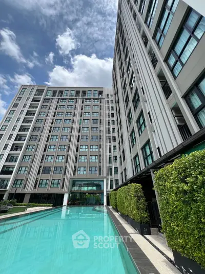 Luxurious modern apartment building with stunning pool and lush greenery under a clear blue sky.