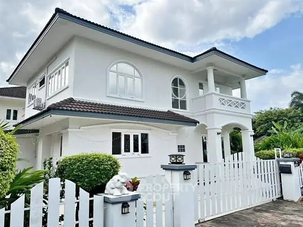 Charming white two-story house with elegant balcony and lush greenery