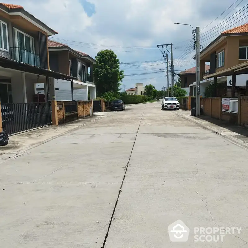 Charming residential street lined with modern houses and lush greenery under a clear blue sky, offering a serene suburban living experience.