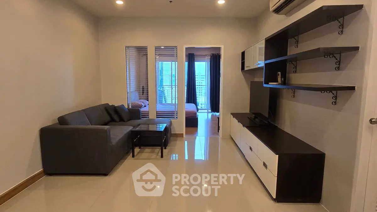Modern living room with sleek furniture and open view to bedroom