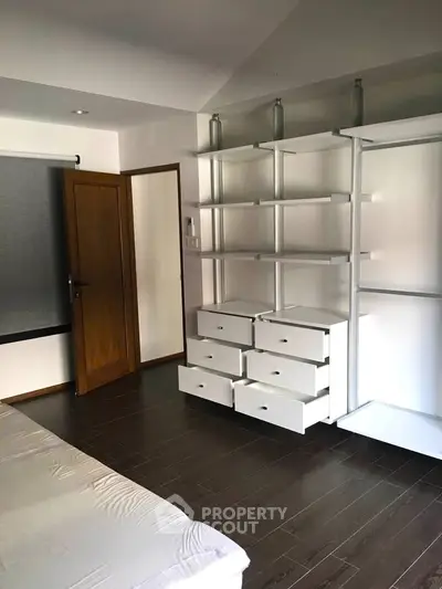 Spacious bedroom with modern shelving and dark wood flooring