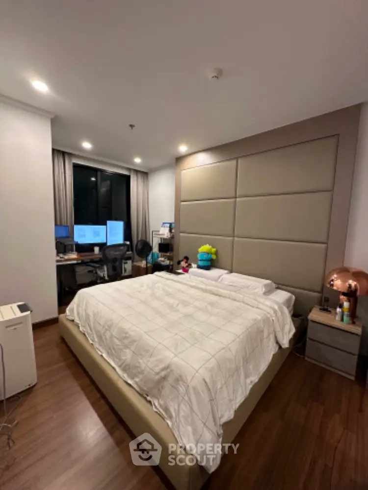 Spacious bedroom with large bed and modern home office setup, featuring elegant wood flooring and ambient lighting.