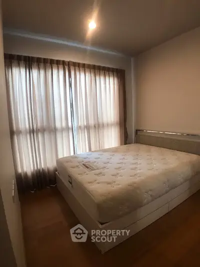 Cozy bedroom with natural light and elegant curtains, featuring a comfortable bed and wooden flooring.
