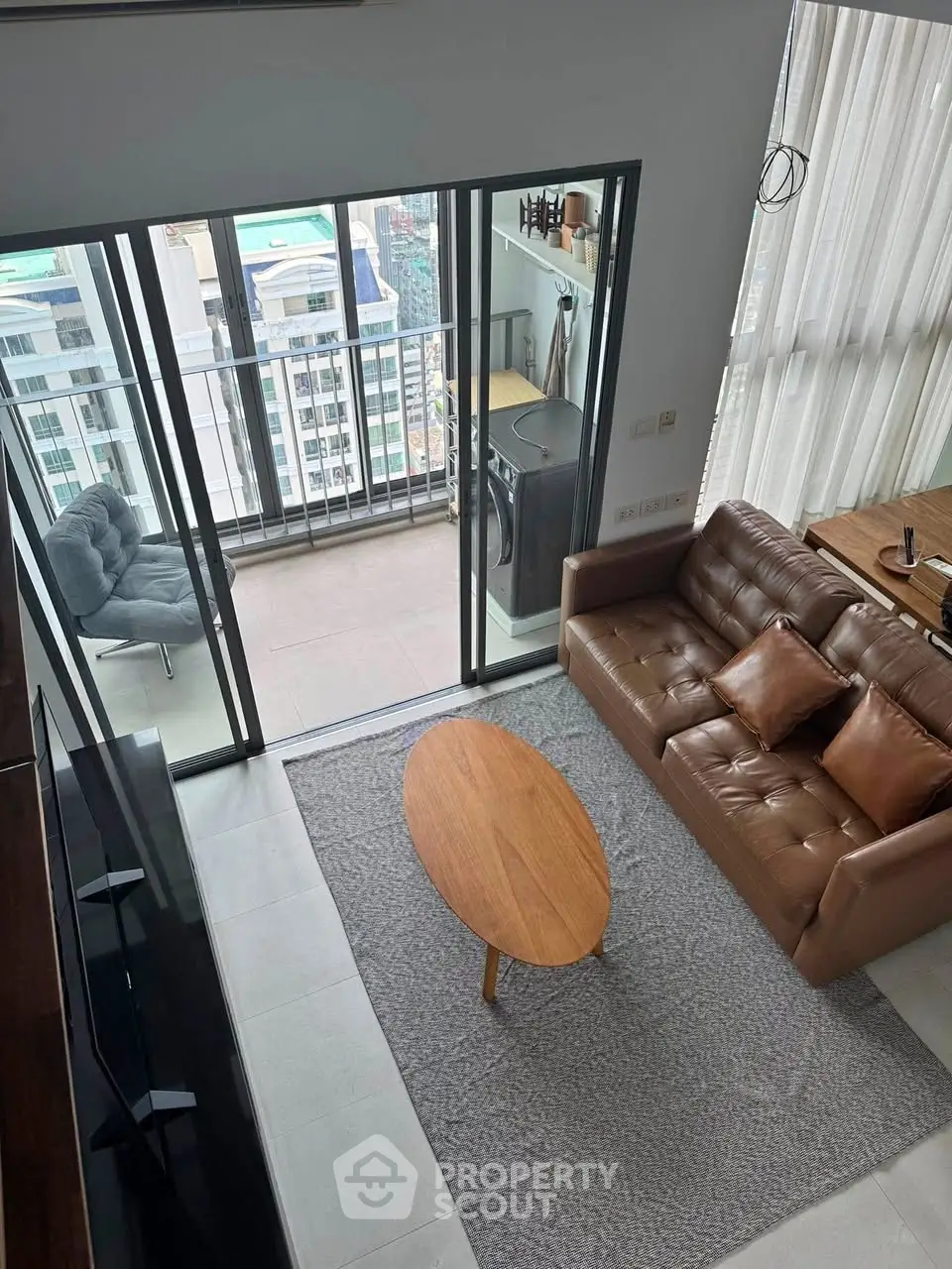 Modern living room with balcony view, featuring leather sofa and stylish decor in high-rise apartment.