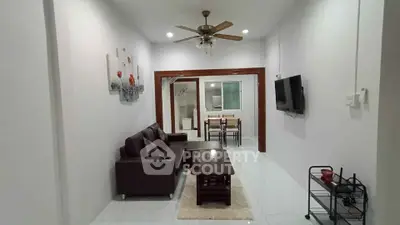 Spacious living room with modern furniture and ceiling fan, leading to a dining area.