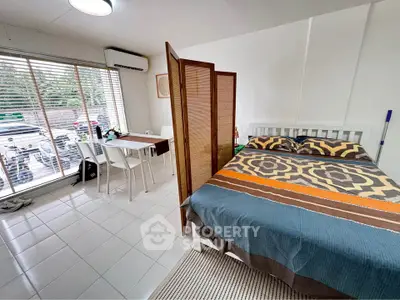 Cozy studio apartment with bed, dining area, and large window for natural light.