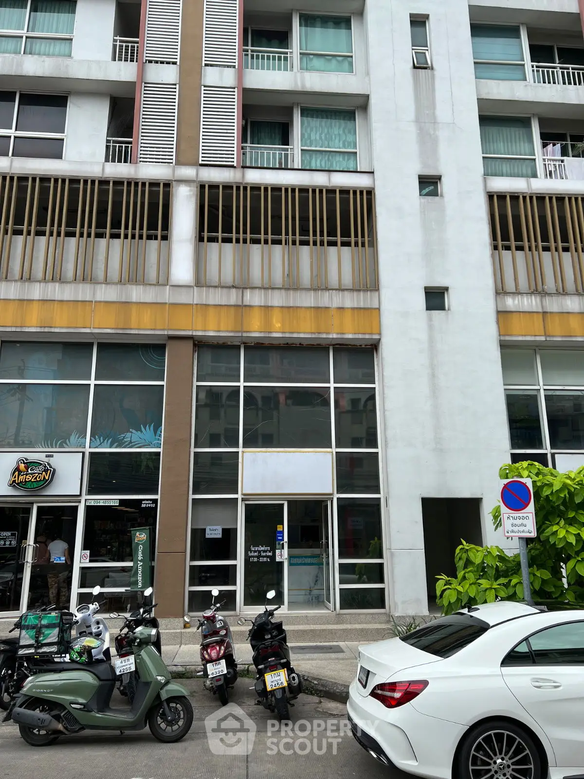 Modern urban building exterior with street-level shops and parked vehicles.