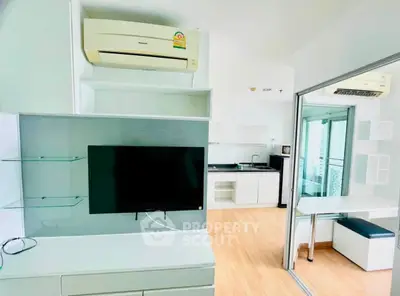Modern living room with sleek TV setup and compact kitchen in open layout apartment.