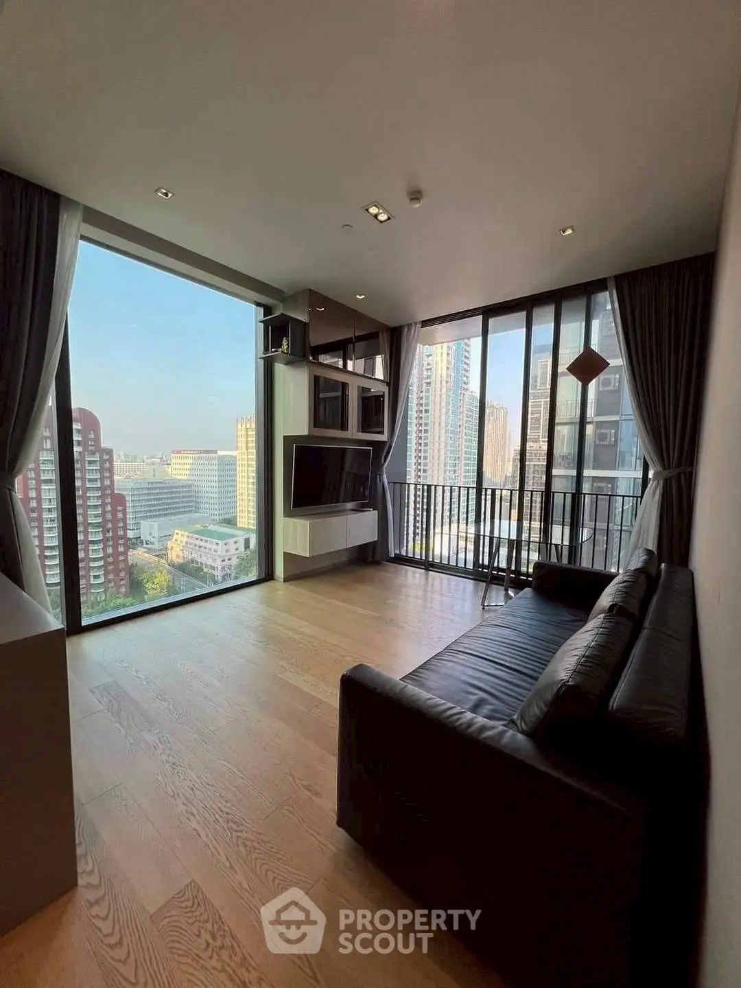 Modern living room with large windows and stunning city view, featuring sleek black sofa and wooden flooring.