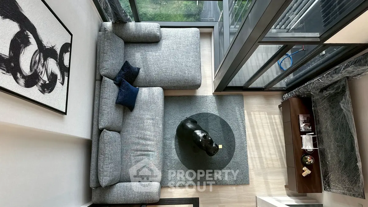 Modern living room with large windows, stylish gray sofa, and contemporary decor in a high-rise apartment.