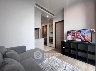 Modern living room with cozy gray sofa, stylish TV setup, and sleek open kitchen design.