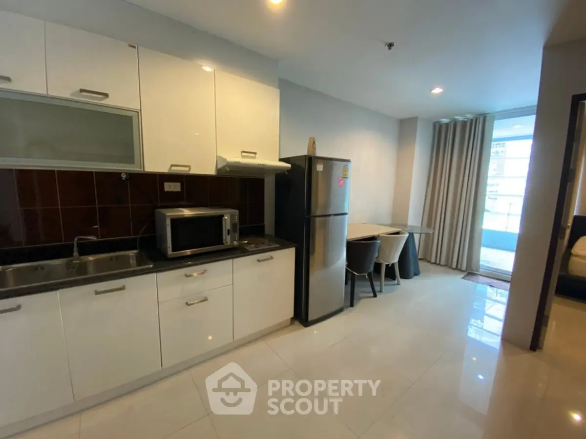 Modern kitchen with sleek cabinets, stainless steel fridge, and dining area in open layout apartment.
