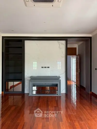 Elegant living room with polished wooden floors and built-in shelving, featuring a modern fireplace and marble accent wall.