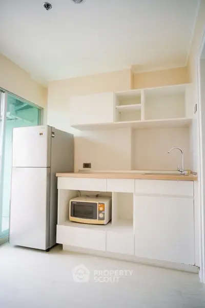 Modern kitchen with sleek white cabinets and appliances, featuring a microwave and fridge.
