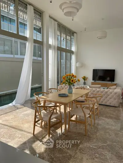 Spacious living room with elegant dining area and large windows, featuring modern furniture and abundant natural light.