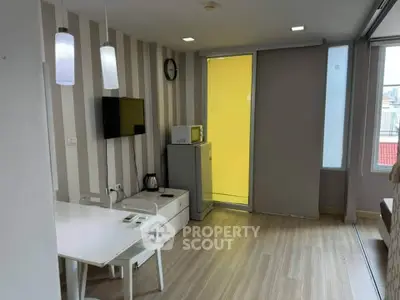 Modern living room with stylish decor and natural light, featuring a compact dining area and wall-mounted TV.