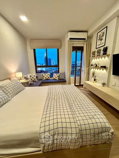 Modern bedroom with city view, stylish decor, and cozy seating area.