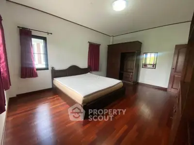 Spacious bedroom with wooden flooring and large bed in a serene setting.