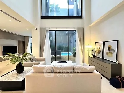 Luxurious modern living room with high ceilings and pool view, featuring elegant decor and natural light.