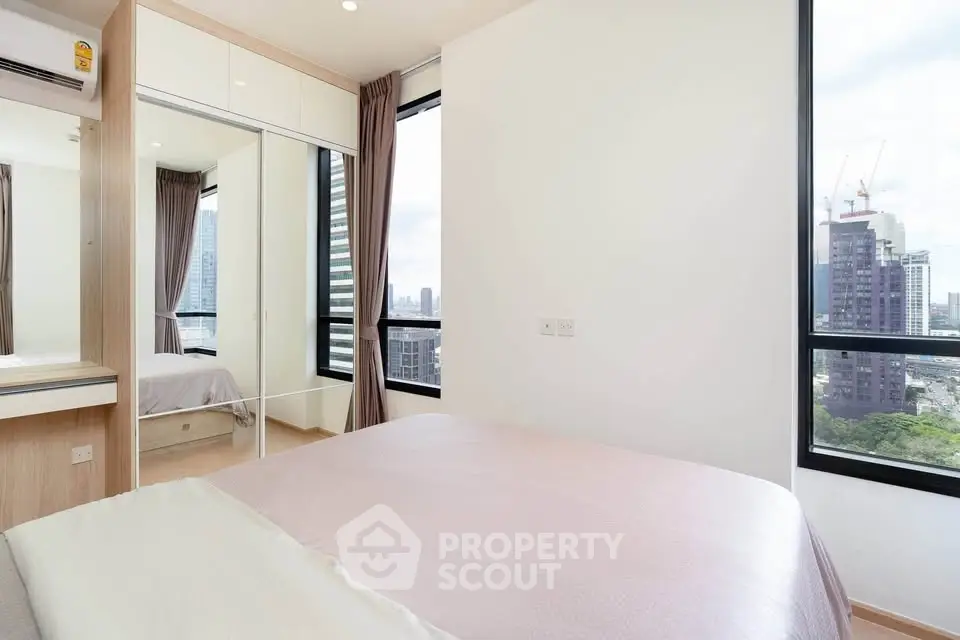 Modern bedroom with city view, featuring large windows and sleek mirrored wardrobe.