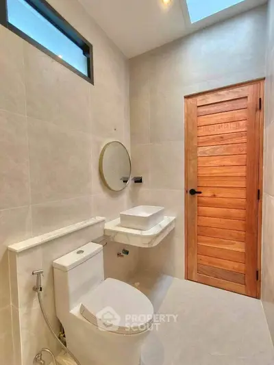 Modern bathroom with sleek fixtures and wooden door, featuring a round mirror and skylight.