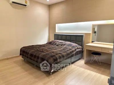 Modern bedroom with stylish bed and wooden flooring, featuring a sleek vanity and ambient lighting.
