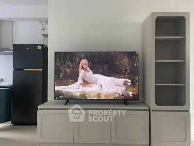 Modern living room with sleek TV unit and stylish shelving, adjacent to a contemporary kitchen with black fridge.