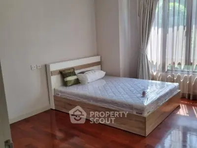 Bright bedroom with wooden flooring and large window, featuring a comfortable bed.
