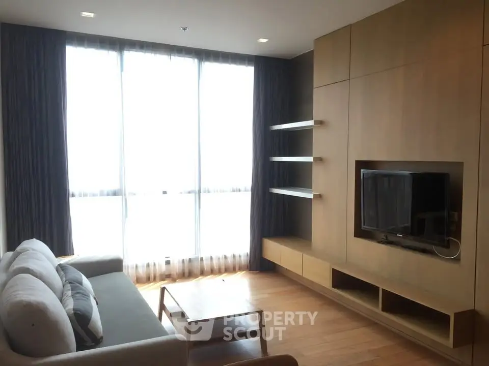 Modern living room with large windows and built-in TV unit, featuring a cozy sofa and wooden flooring.