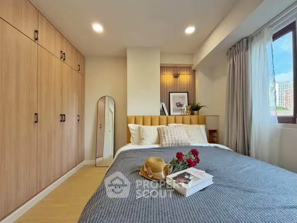 Cozy bedroom with modern decor, large wardrobe, and natural light from window.