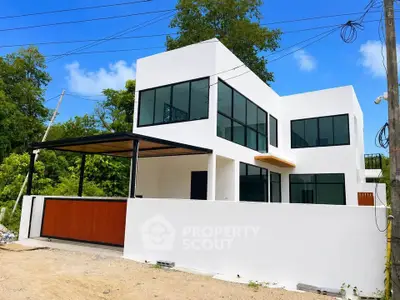 Modern minimalist white house with large windows and a covered patio, surrounded by lush greenery.