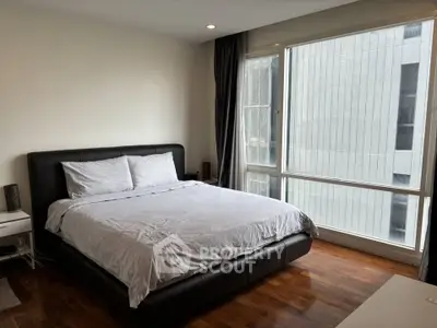 Spacious bedroom with large window and modern furnishings in a high-rise apartment.