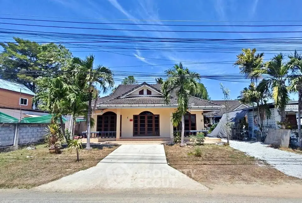 Charming single-story house with palm trees and spacious driveway under clear blue sky.