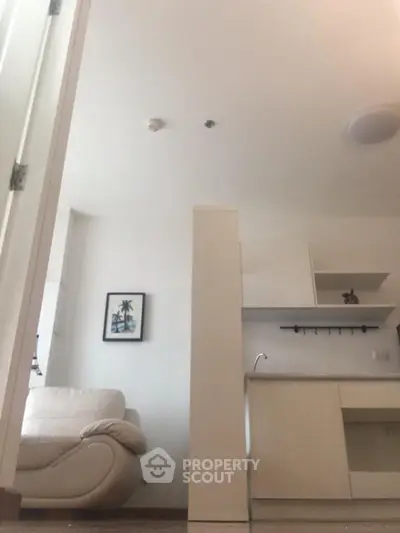 Modern apartment interior with open kitchen and cozy living area, featuring sleek white cabinetry and comfortable seating.