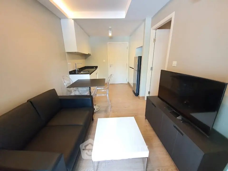 Modern living room with sleek black sofa, TV, and open kitchen layout in a stylish apartment.